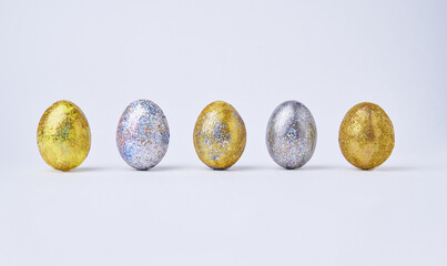 Golden and silver shiny painted eggs on white background.