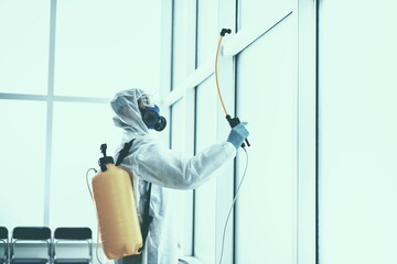 disinfector in a protective suit is spraying a disinfectant in the room.