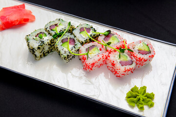 California maki sushi with caviar. Roll made of crab meat, svocado, cucumber inside. Served on a white plate.
