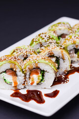 Uramaki sushi roll with smoked eel and unagi on white plate over black background. Japanese cuisine concept.