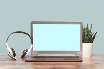 Front view of laptop mockup screen with headphones on wooden desk. Blue background. Distant learning. working from home, online courses or support. Audio podcast. Helpdesk or call center headset - obrazy, fototapety, plakaty