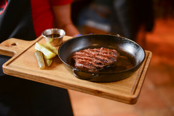 Succulent thick juicy grilled fillet steak served on an old wooden board by waiter in restauratn or diner.