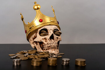 A skull with a crown on its head against a gray background lies next to a pile of gold coins.