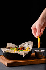 Fried potatoes in an iron pan over rustic wooden board and black background. Rustic style dinner.
