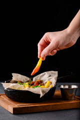Fried potatoes in an iron pan over rustic wooden board and black background. Rustic style dinner.