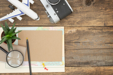 Travel wooden background with accessories for trip - photo camera, plane, map, sheet of paper, pen, magnifier, houseplant and place for text