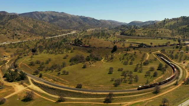 A long train stretches the full length of the Tehachapi Loop spiral - slow motion aerial view