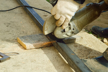 close-up - worker cuts a metal profile with a grinder, hands in protective white gloves