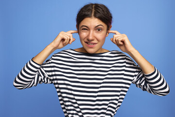 Horizontal shot of displeased teenage girl wearing septum ring having clogged ears, trying to...