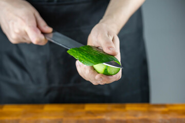 Close up of Chef cook hands chopping vegetables for traditional Asian cuisine with Japanese knife. Professional Sushi chef cutting cucumber for rolls.