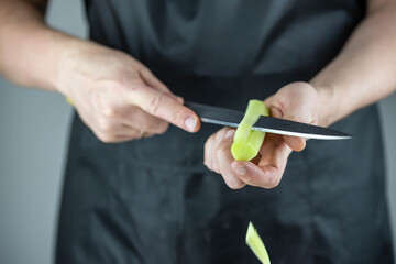 Close up of Chef cook hands chopping vegetables for traditional Asian cuisine with Japanese knife. Professional Sushi chef cutting cucumber for rolls.