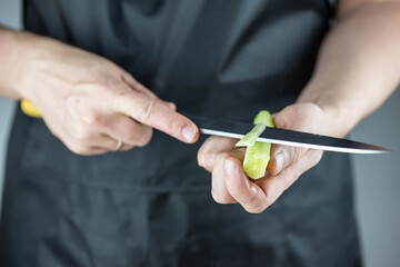 Close up of Chef cook hands chopping vegetables for traditional Asian cuisine with Japanese knife. Professional Sushi chef cutting cucumber for rolls.