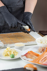 Close up of sushi chef hands preparing japanese food. Man cooking sushi at restaurant. Traditional asian seafood rolls on cutting board.