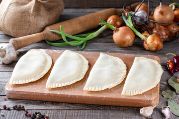 Raw chebureks on a wooden background. The concept of home baking with raw dough and minced meat