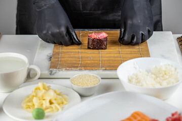 Close up of sushi chef hands preparing japanese food. Man cooking sushi at restaurant. Traditional asian seafood rolls on cutting board.