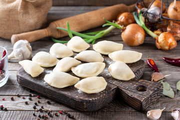 Fototapeta na wymiar The process of making home-made dumplings. Molding dumplings. Raw homemade dumplings on a wooden board.