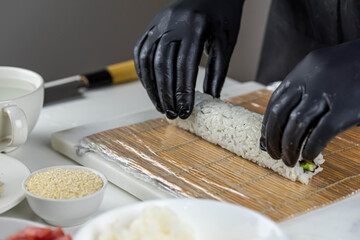 Close up of sushi chef hands preparing japanese food. Man cooking sushi at restaurant. Traditional asian seafood rolls on cutting board.