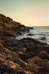 Fototapeta na wymiar Rocks around the blue water at Golden Bay during golden hour on a warm fall day in Malta.