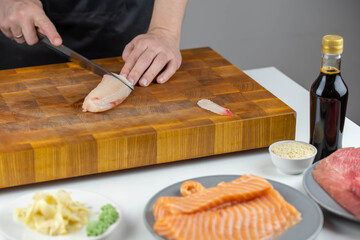Obraz premium Close up of Chef cook hands chopping salmon fish for traditional Asian cuisine with Japanese knife. Professional Sushi chef cutting seafood for rolls.