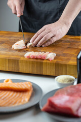 Close up of Chef cook hands chopping salmon fish for traditional Asian cuisine with Japanese knife. Professional Sushi chef cutting seafood for rolls.