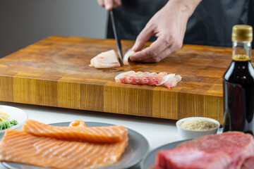 Close up of Chef cook hands chopping salmon fish for traditional Asian cuisine with Japanese knife. Professional Sushi chef cutting seafood for rolls.