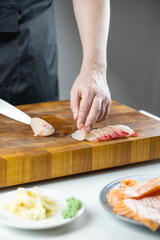 Close up of Chef cook hands chopping salmon fish for traditional Asian cuisine with Japanese knife. Professional Sushi chef cutting seafood for rolls.