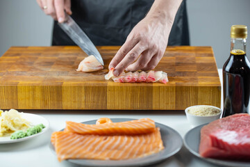 Close up of Chef cook hands chopping salmon fish for traditional Asian cuisine with Japanese knife. Professional Sushi chef cutting seafood for rolls.