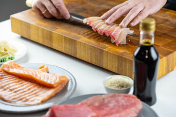 Close up of Chef cook hands chopping salmon fish for traditional Asian cuisine with Japanese knife. Professional Sushi chef cutting seafood for rolls.