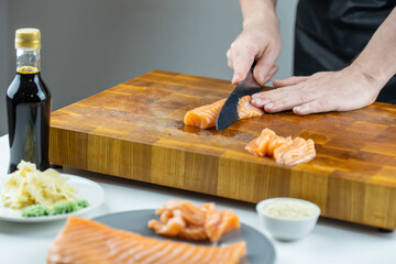 Close up of Chef cook hands chopping salmon fish for traditional Asian cuisine with Japanese knife. Professional Sushi chef cutting seafood for rolls.