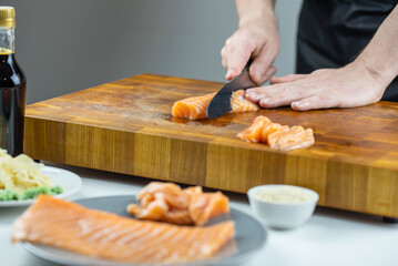 Close up of Chef cook hands chopping salmon fish for traditional Asian cuisine with Japanese knife. Professional Sushi chef cutting seafood for rolls.