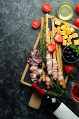 Board with grissini and snacks, and wine on black smokey table