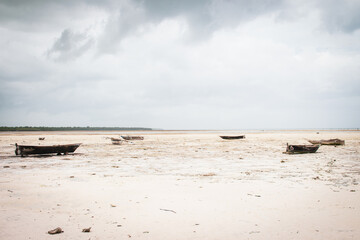 Wooden boats on low tide, toned. Zanzibar beach with old nautical vessel. African seascape with cloudy sky. Empty coast of Indian Ocean, Tanzania. Boats on the beach. Summer vacation concept. 