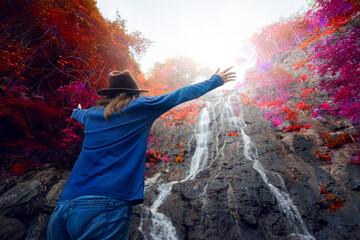 Amazing adventure young traveller woman happy on the mountain with the waterfall at colorful autumn forest.