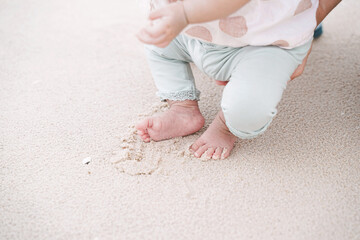 Fototapeta na wymiar Little foot of baby girl on sandy beach. Walking on sand for the first time.