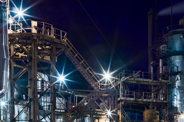 Night industrial petrochemical landscape. Reactors pipes stairs and columns. Large-capacity production enterprise workshop. Petrochemical plant, reactors and converters under dark sky with copyspace.