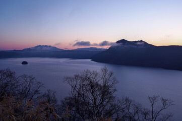 夜明けの湖とその周りの山並みのシルエット。の本の北海道の摩周湖。