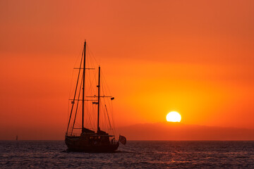 Fototapeta premium Silhouette of sailing boat with sails down against sun at sunset, sun glare on sea waters. Romantic seascape. Holiday lifestyle landscape 