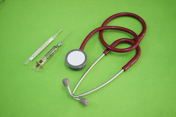 Stethoscope, thermometer and syringes of doctor on green background in clinic.