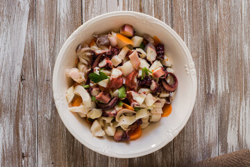 Seafood salad dressed and served in porcelain bowl on wooden background