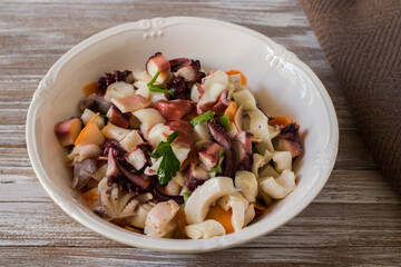 Seafood salad dressed and served in porcelain bowl on wooden background