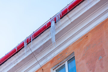 Icicles hanging from the roof of an apartment building in winter. Close-up