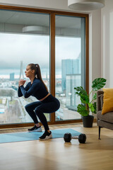 Slender brunette in jumpsuit practices squats near window