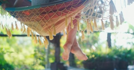 Young woman sits in the hammock on a balcony in a tropical garden