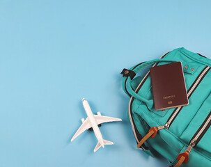  flat lay of passport, green backpack  and airplane model on blue background. Traveling concept.