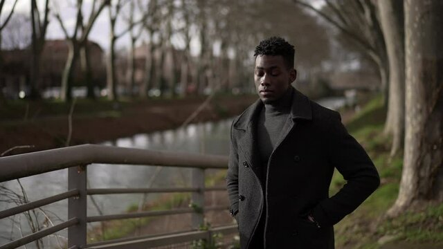 Elegant young black man standing outside at park wearing winter clothing coat