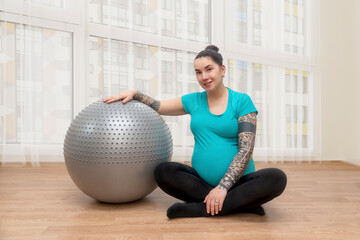 A pregnant woman  is engaged in fitness with fitball at home at the panoramic window.