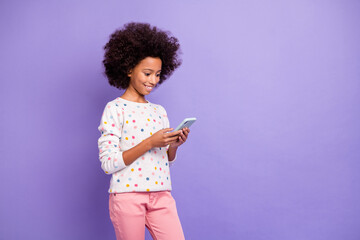 Photo of brown haired small afro american girl wear pink trousers white sweater read phone isolated on violet color background