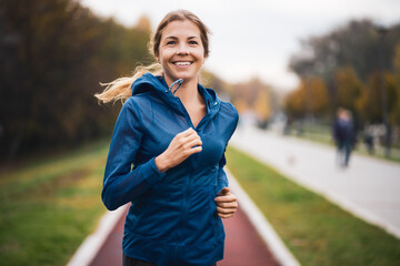 Beautiful adult woman is jogging outdoor on cloudy day in autumn. - obrazy, fototapety, plakaty