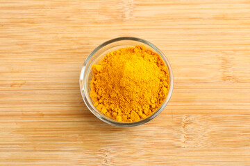 Turmeric powder in glass bowl on wooden background.