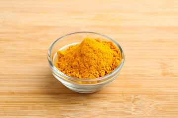 Turmeric powder in glass bowl on wooden background.